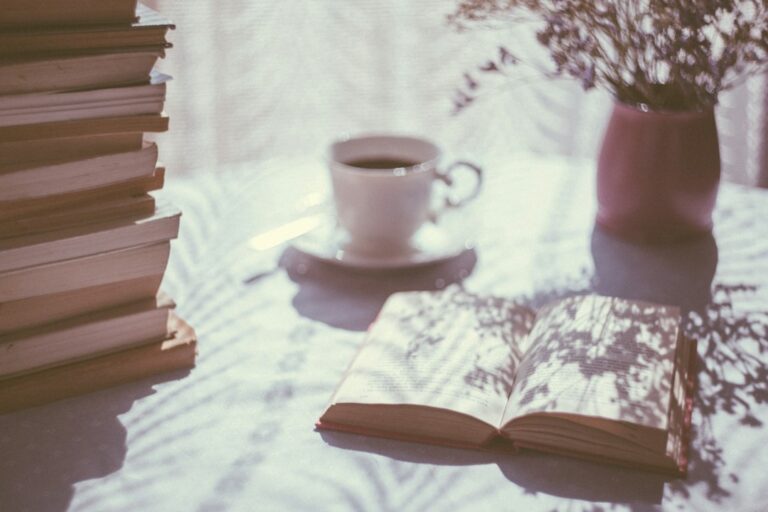 An open book and cup beside a sunlit window.