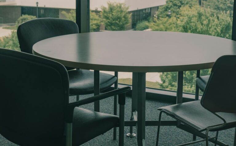 Empty chairs around a round table beside a large window.