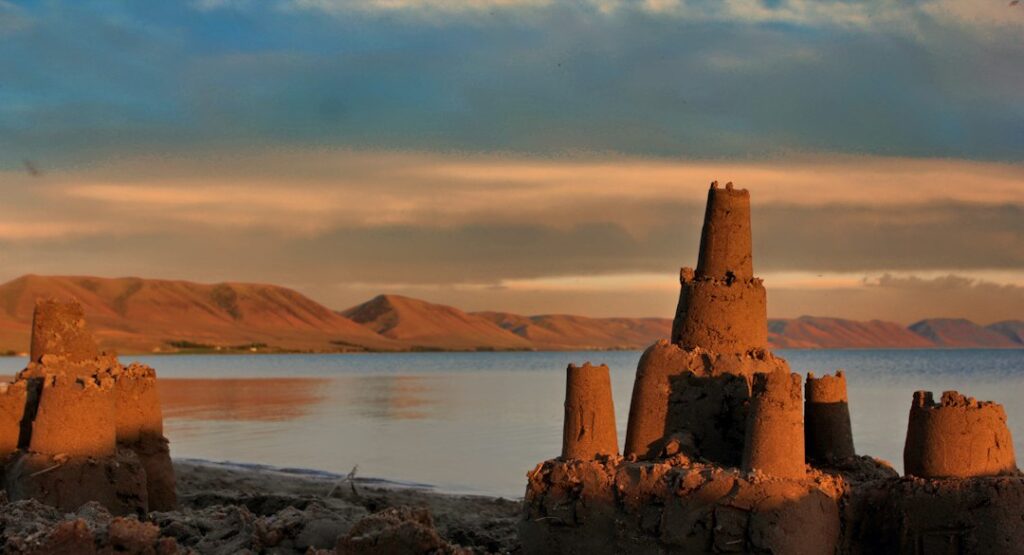 Sandcastles beside a lake in evening light.
