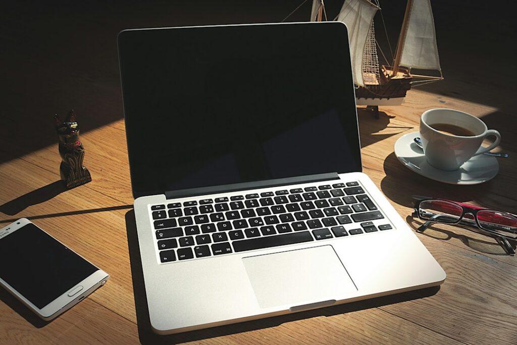 A laptop, phone and coffee cup on a desk after dark.