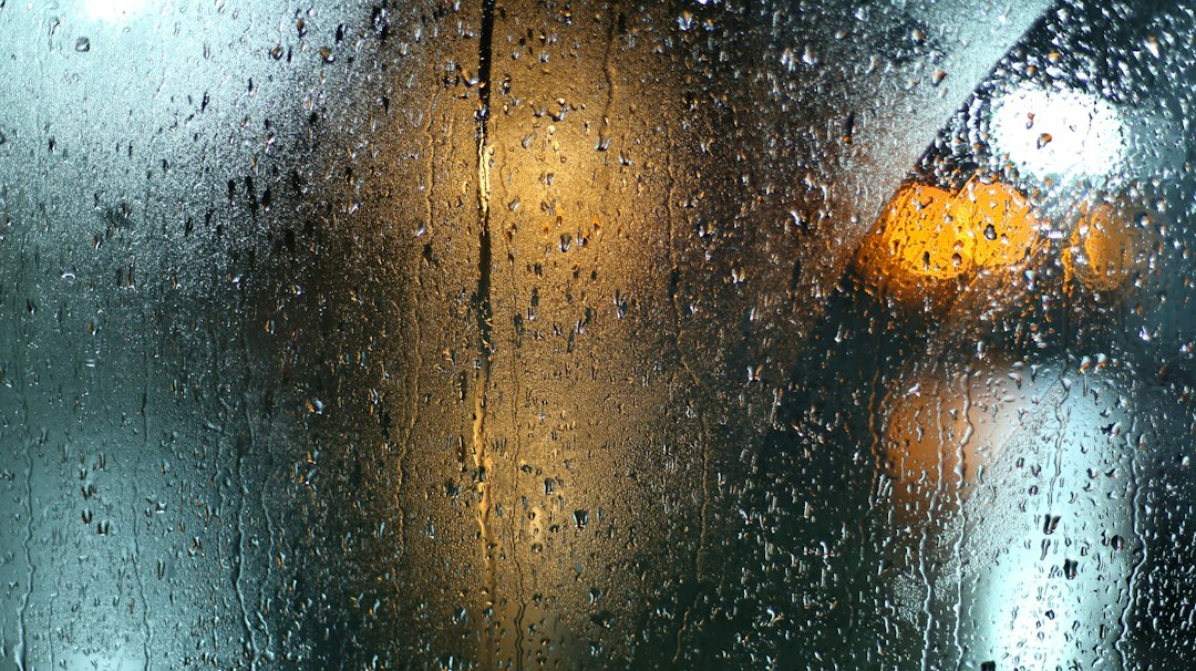 Raindrops on a window with softly blurred lights beyond it.